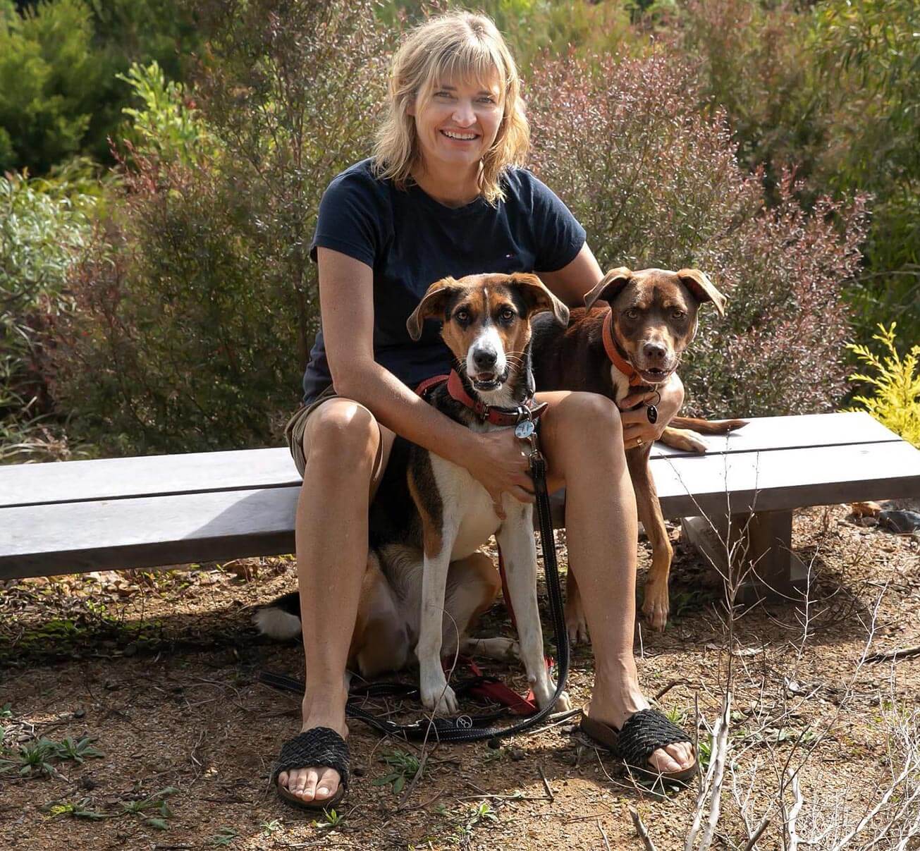 woman sitting on a bench with two dogs smiling